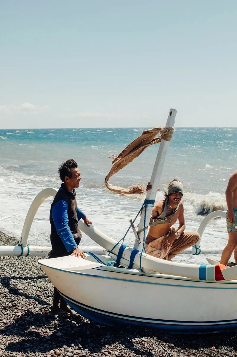 Two fishermen pushing a wooden jukung out through the surf at Tianyar