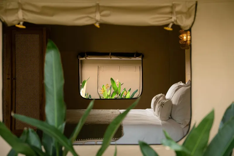 Inside a canvas lodge: the bed under the canvas roof, a woven screen and a window onto the garden