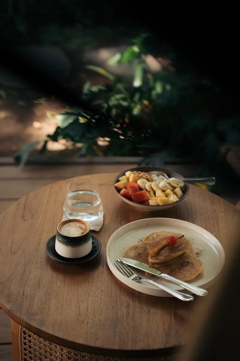 Breakfast at a round wooden table at Saga: coffee, fruit and pancakes.