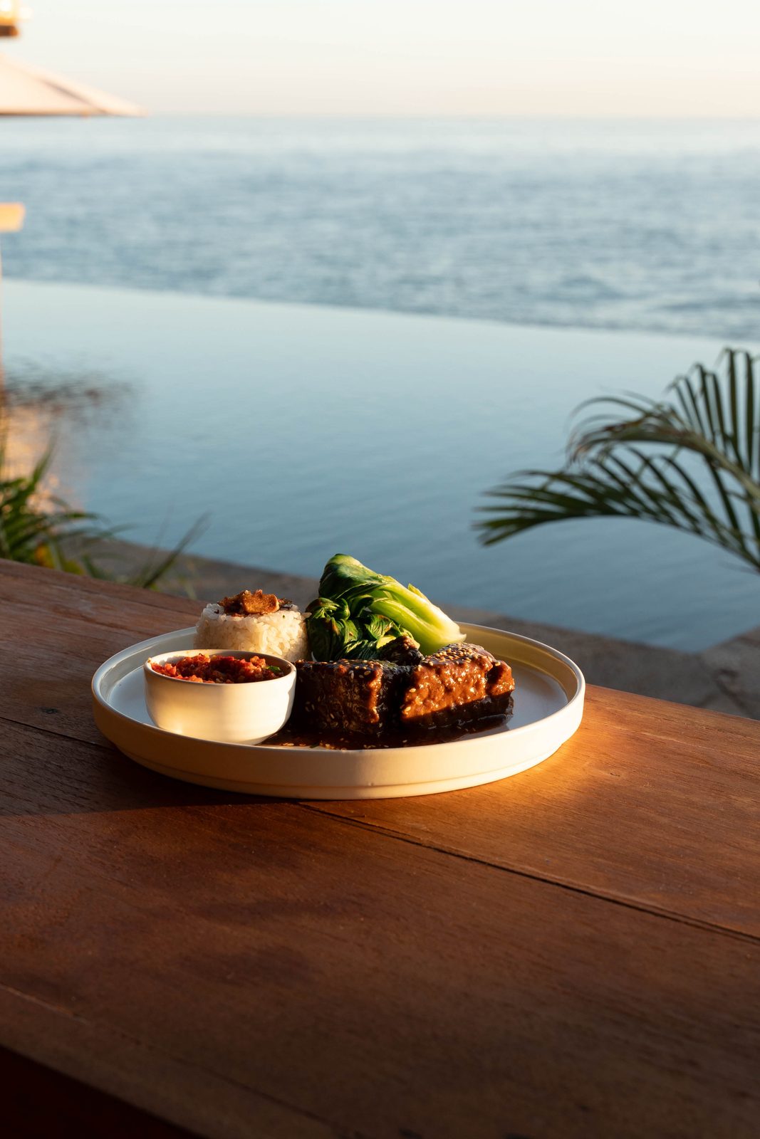 A plate at the Saga table in low sun, the pool and the sea behind it