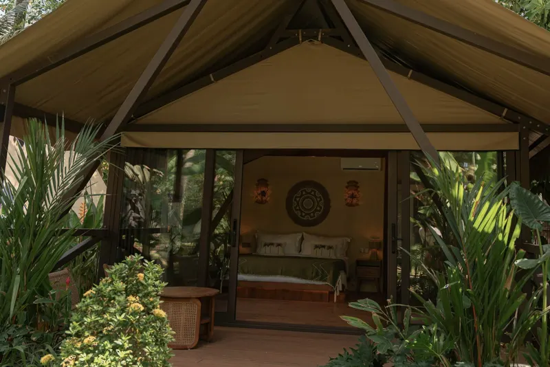 Segara from the front: a canvas lodge with a pointed roof and a glass front, a bed visible inside, tropical plants on both sides