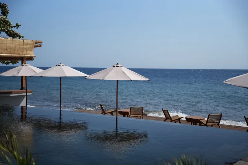 The pool at VELA Tianyar with parasols and loungers, the sea directly behind it