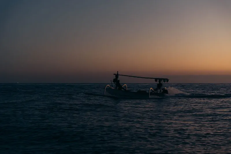 Two fishermen in a wooden jukung on open water off Tianyar, the sun low and spray off the bow
