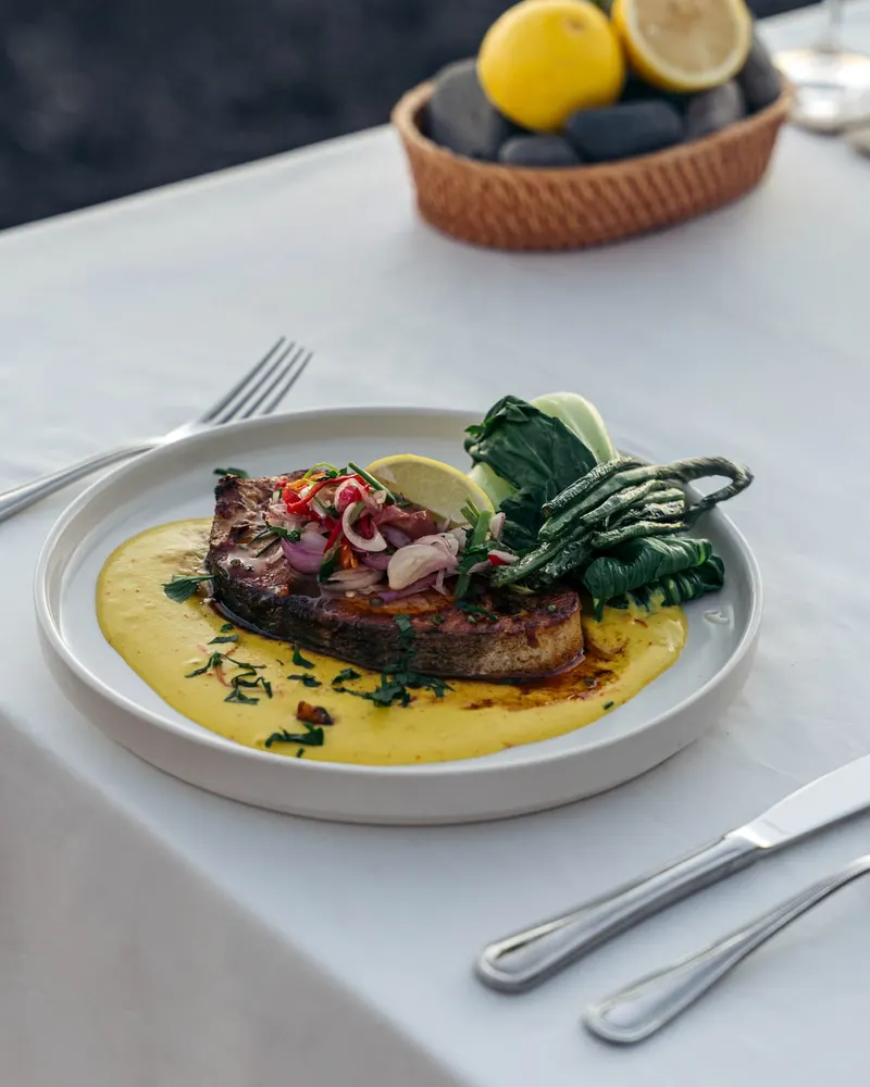 A grilled fish with sambal matah, coastal greens and lime on a white cloth at Saga