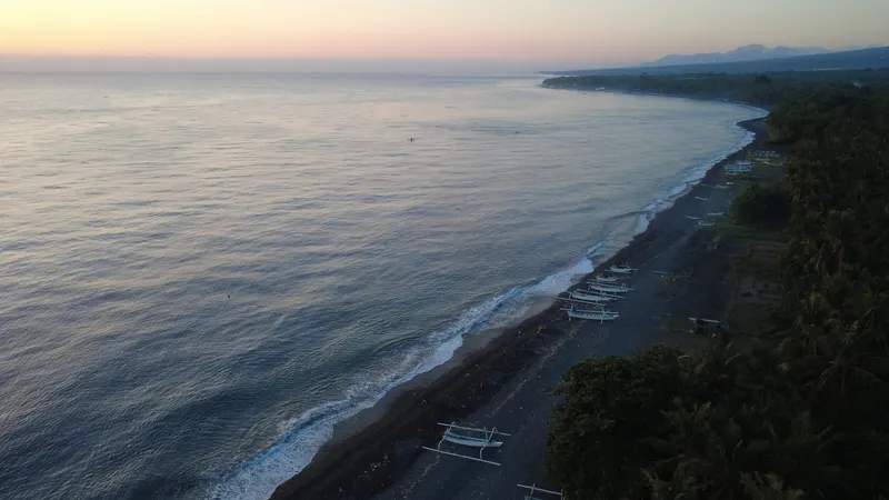 First light over a calm sea off the Tianyar coast, fishing boats resting in shadow near the shore