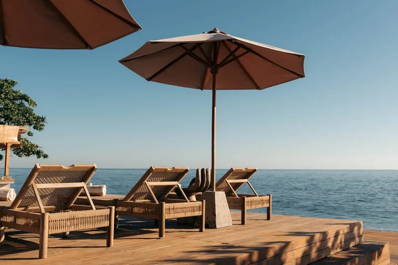 Wooden sun loungers and two parasols on a timber deck, the sea beyond its edge.