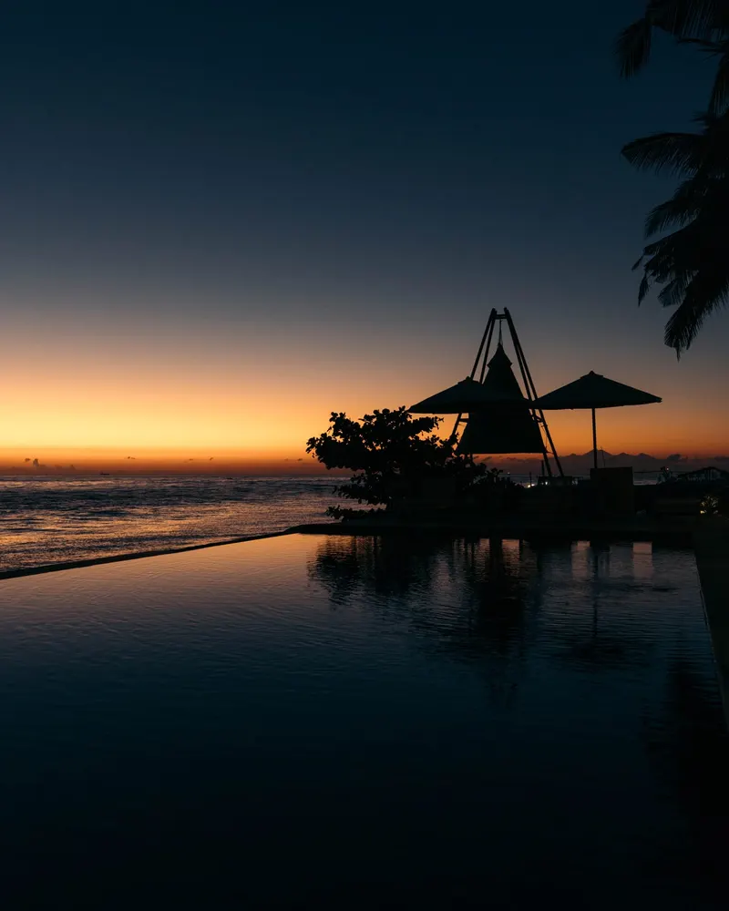 Saga's roofline and the palms silhouetted over the pool after sunset, the last light on the water