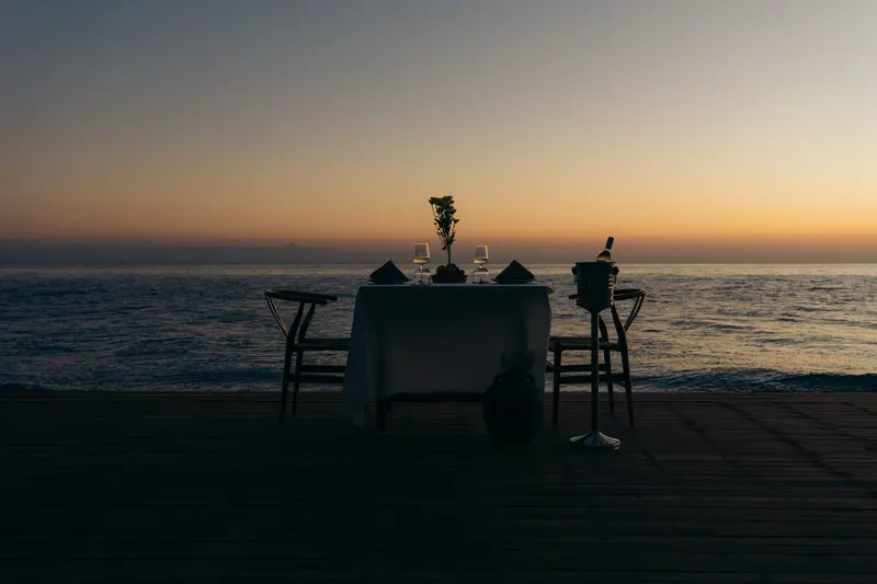 A table for two on the deck at the shore at dusk, the sky still lit over the sea