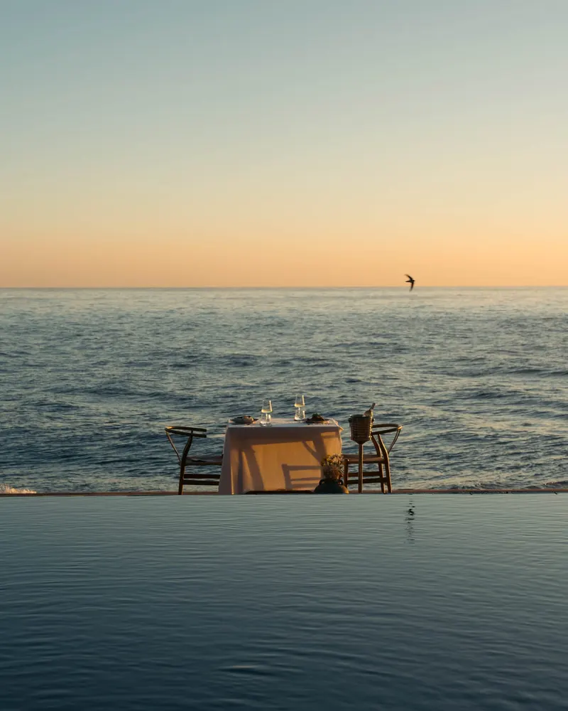 A table for two with a white cloth at the pool edge at Saga, the sea beyond, in evening light